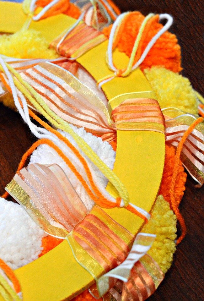 Bright, fluffy and Halloween-happy, Candy Corn Pompom Wreaths are candy-inspired holiday decor for doors or windows! At littlemisscelebration.com #crafts #halloween