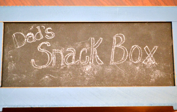 A small wooden crate that’s pre-painted with a chalkboard front makes it a snap to put together this Easy Snack Crate for Dad! Fill with his favorite munchies! at littlemisscelebration.com